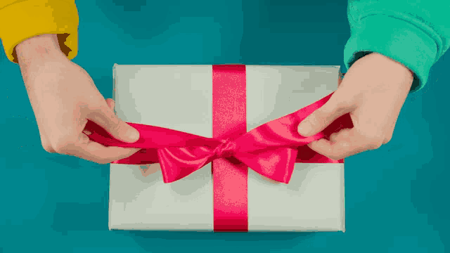 a person is tying a pink bow on a white gift box