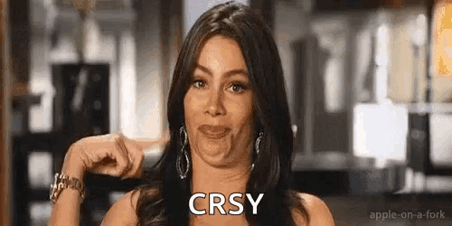 a woman is making a funny face and pointing at herself with the word crsy on her face .