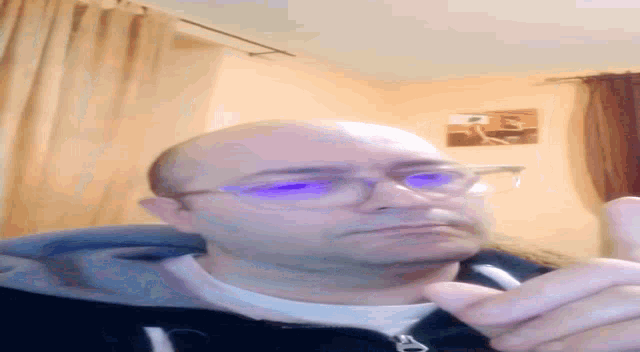 a bald man wearing glasses and a black jacket looks down at something