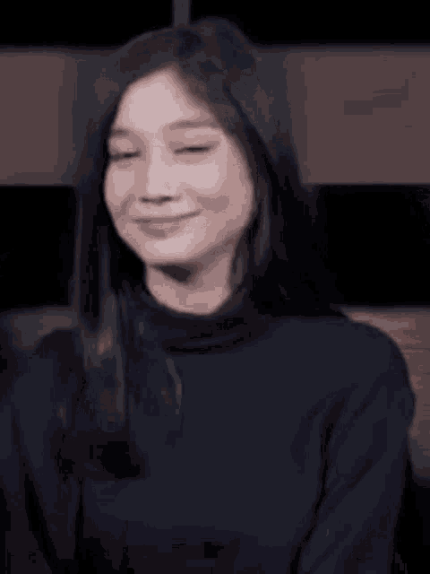 a woman in a black turtleneck sweater is smiling and making a heart shape with her hands .