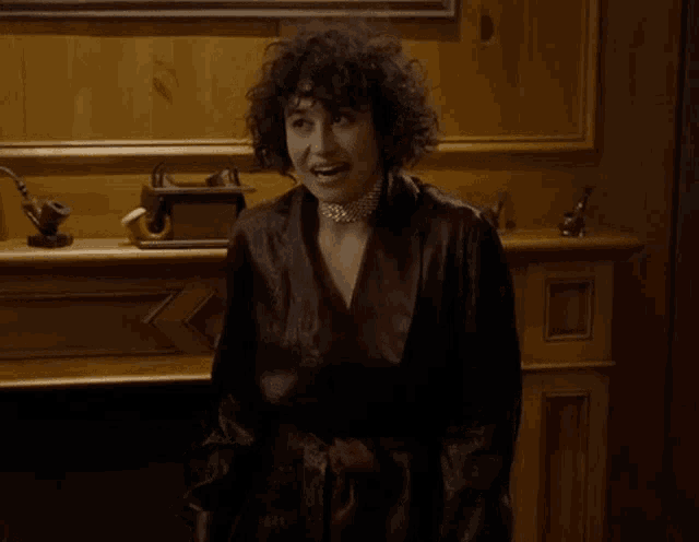 a woman with curly hair is standing in front of a fireplace wearing a robe