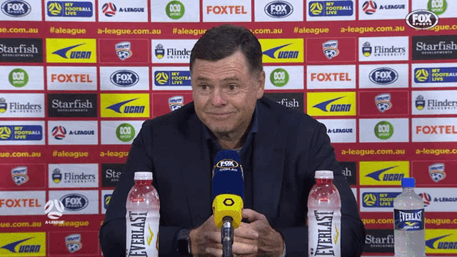 a man speaking into a microphone in front of a fox advertisement board