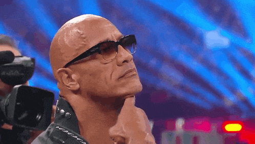 a bald man wearing sunglasses holds his hand to his ear .
