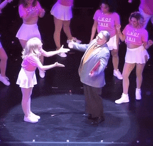 a group of people are dancing on a stage and one of the girls is wearing a shirt that says i go this