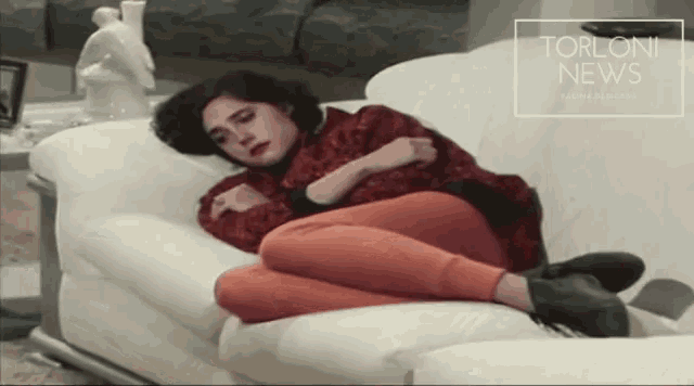 a woman is laying on a white couch with a torloni news logo in the corner