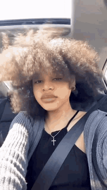 a woman with a large afro is sitting in a car wearing a seat belt and a necklace with a cross .