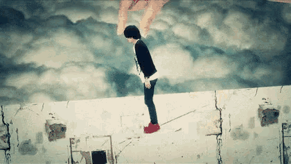 a person is standing on top of a concrete wall with a painting of a hand reaching out towards them .