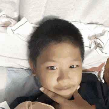 a young boy is laying on a bed with his hand on his face