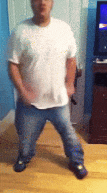 a man in a white shirt and blue jeans is dancing in front of a tv