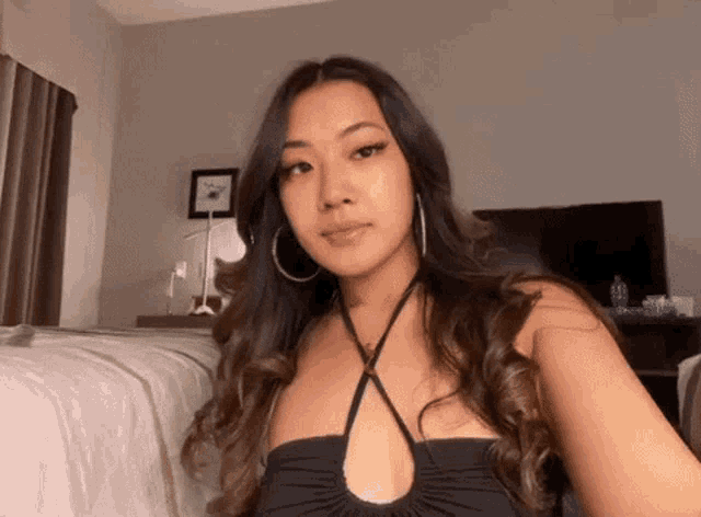 a woman wearing a black top and hoop earrings takes a selfie in a bedroom