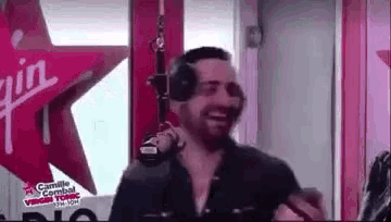 a man wearing headphones is standing in front of a microphone in a studio .