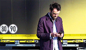 a man in a purple jacket is looking at his phone in front of a truck that says 80-90