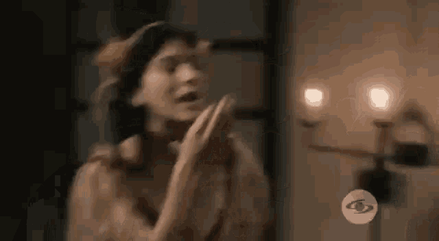a woman is standing in a dark room with her hands in the air and a candle in the background .