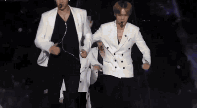 a group of men are dancing on a stage and one is wearing a white jacket