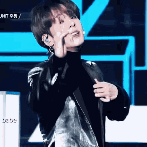 a young man wearing a leather jacket and a black turtleneck is standing on a stage and making a funny face .