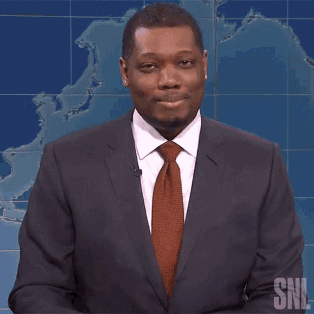 a man in a suit and tie is smiling in front of a snl logo