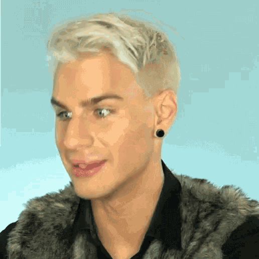 a man with blonde hair and black earrings is wearing a fur vest and a black shirt