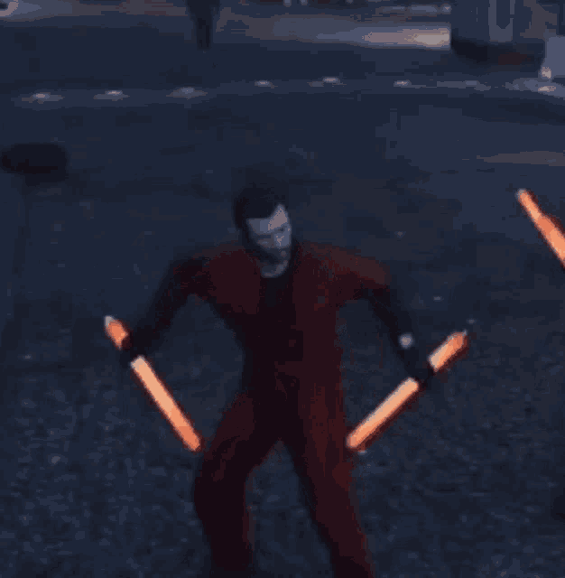 a man in red pants is holding two orange lightsabers .