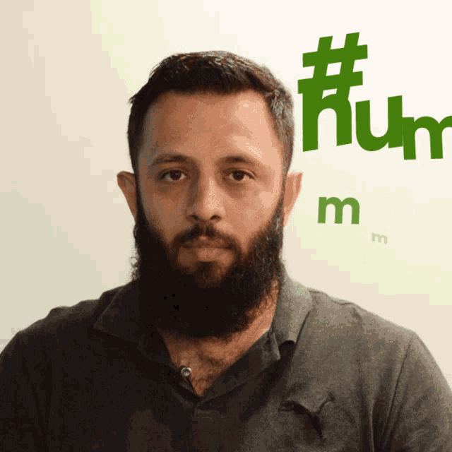 a man with a beard is standing in front of a wall that says #humm