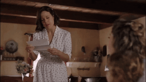 a woman in a white robe is reading a letter to another woman