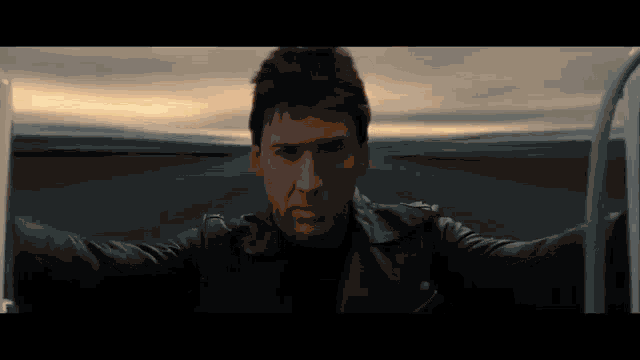 a man in a leather jacket is riding a motorcycle on a highway .