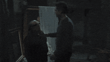 two men are standing in a dark room talking
