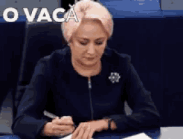 a woman sits at a desk with a pen in her hand and the words o vaca written above her