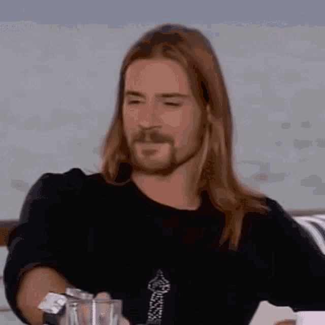 a man with long hair and a beard is sitting at a table .