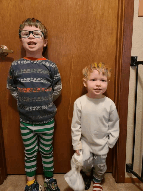 two young boys are standing in front of a wooden door