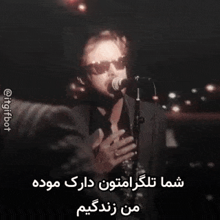a man wearing sunglasses is singing into a microphone in a dark room