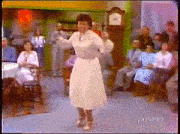 a woman in a white dress is dancing in front of a group of people sitting in chairs and tables