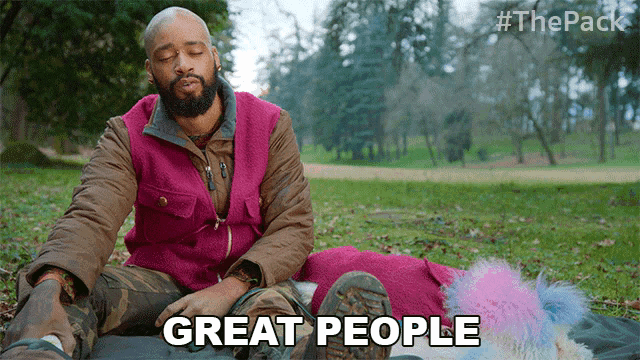 a man in a pink vest is sitting on a blanket in a park and says " great people "