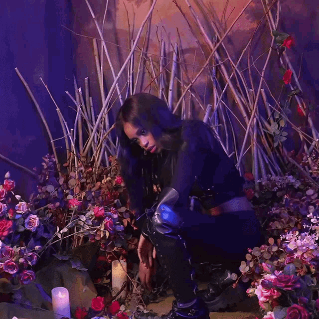 a woman is kneeling down in front of a bunch of flowers and candles