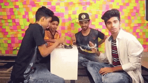 a group of young men are sitting around a table with sticky notes on the wall in the background