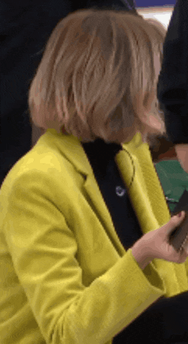 a woman wearing a yellow jacket and black turtleneck holds a wallet