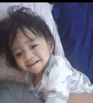 a little girl is smiling while laying on a bed