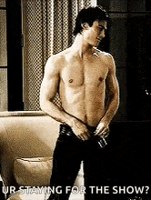 a shirtless man is standing in front of a couch in a room .