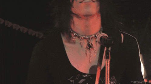 a close up of a person singing into a microphone while wearing a necklace