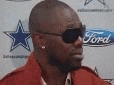 a man wearing sunglasses is standing in front of a ford logo .