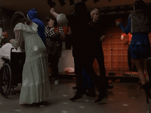 a woman in a white dress is dancing with a man in a wheelchair in the background