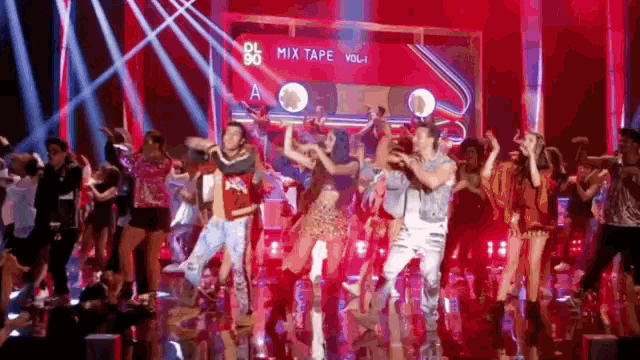 a group of people are dancing on a stage in front of a cassette tape that says mix tape vol 1