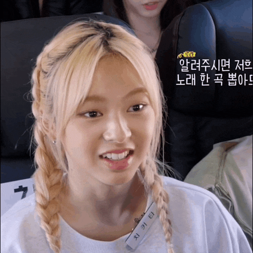 a girl with blonde hair is wearing a name tag that says ' 지 가 단 ' on it