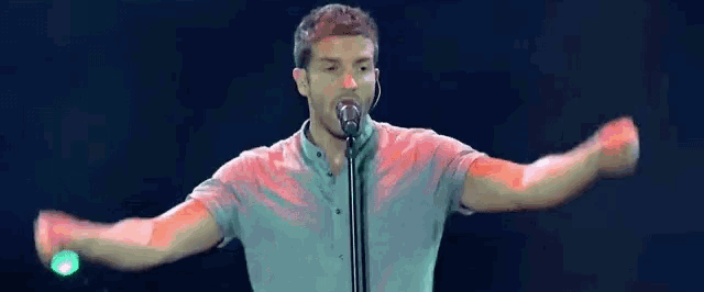 a man singing into a microphone with his arms outstretched in front of him