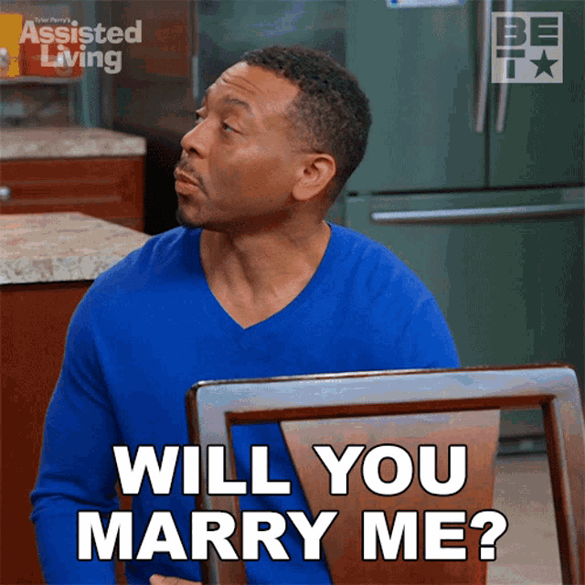 a man in a blue shirt is sitting in a chair and saying will you marry me