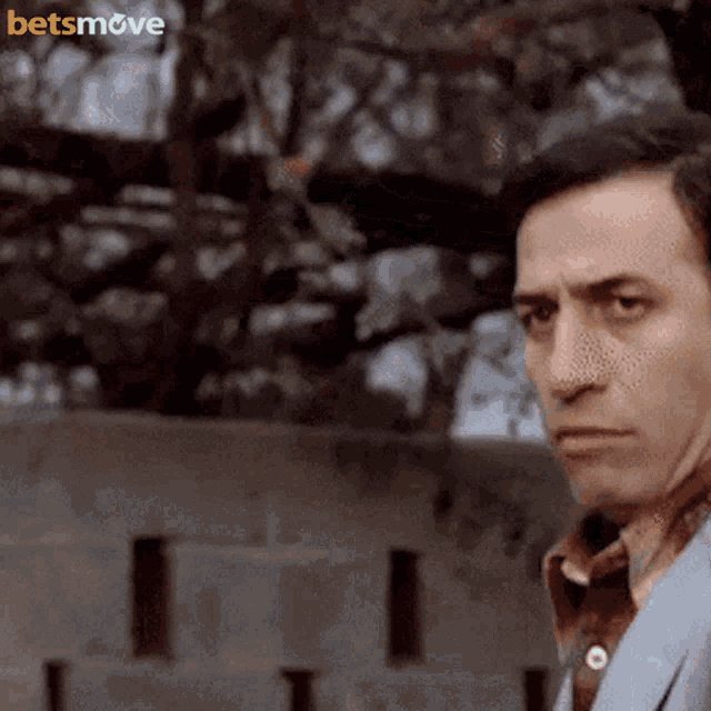 a man in a suit stands in front of a fence with the words betsmove on the bottom