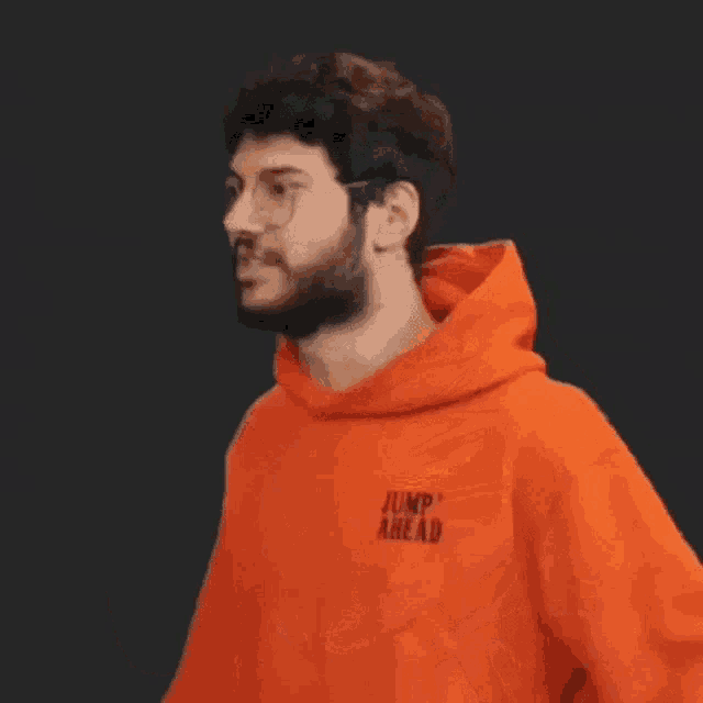 a man with a beard and glasses is wearing an orange hoodie and giving a thumbs up .