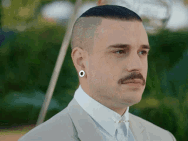 a man with a mustache wearing a suit and earrings .