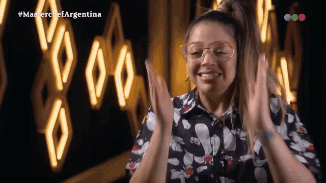a woman wearing glasses is clapping in front of a neon sign that says masterchef argentina