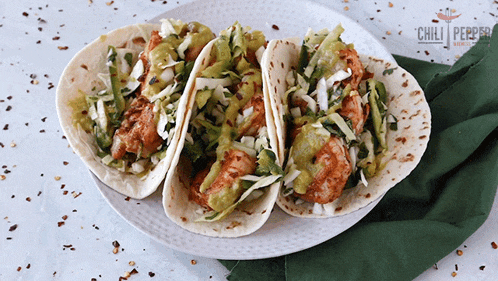 three tacos on a white plate with a chili pepper logo