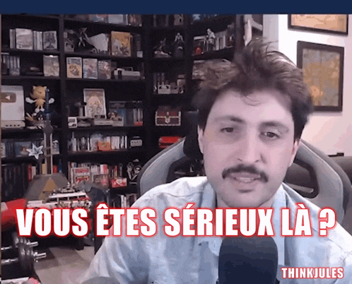 a man with a mustache is sitting in front of a bookshelf and says " vous etes serieux la "